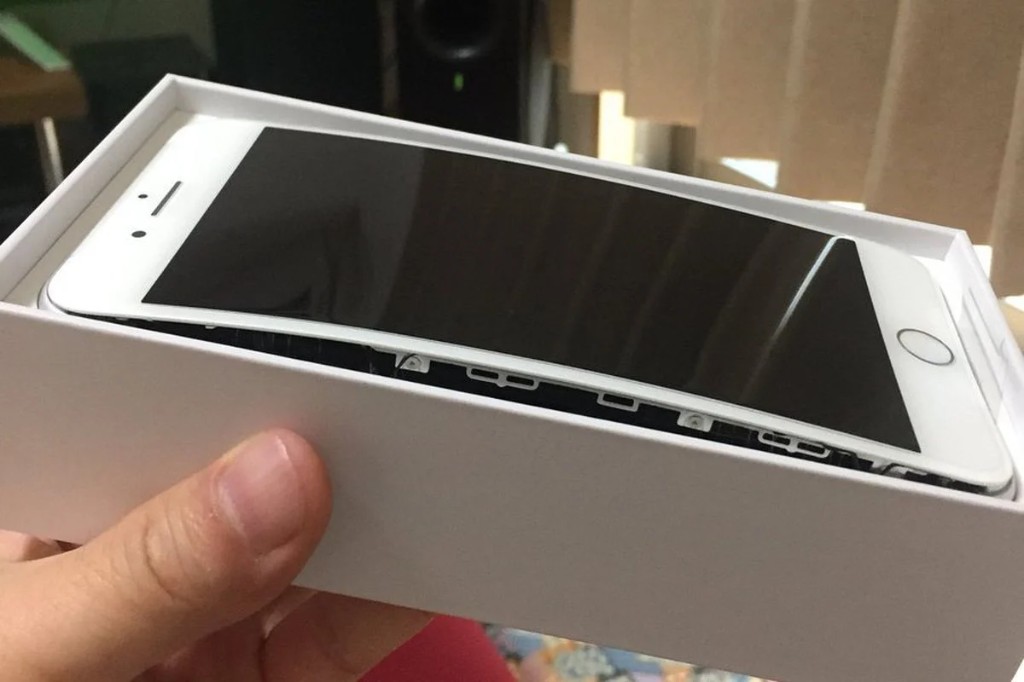 A white phone with its screen lifted out of the frame by a swollen battery, sitting in its retail box