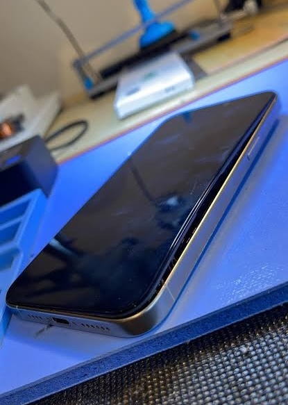 A silver phone on a repair mat with its screen lifting along the edge from a swollen battery